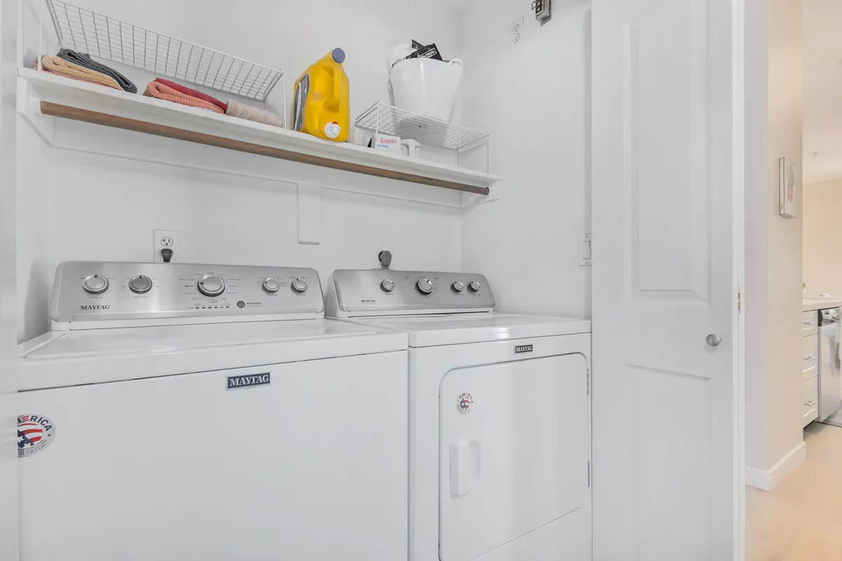 A tidy laundry area with a full-sized washing machine and dryer, laundry supplies neatly arranged on a shelf above—a practical and well-organized space for everyday needs.