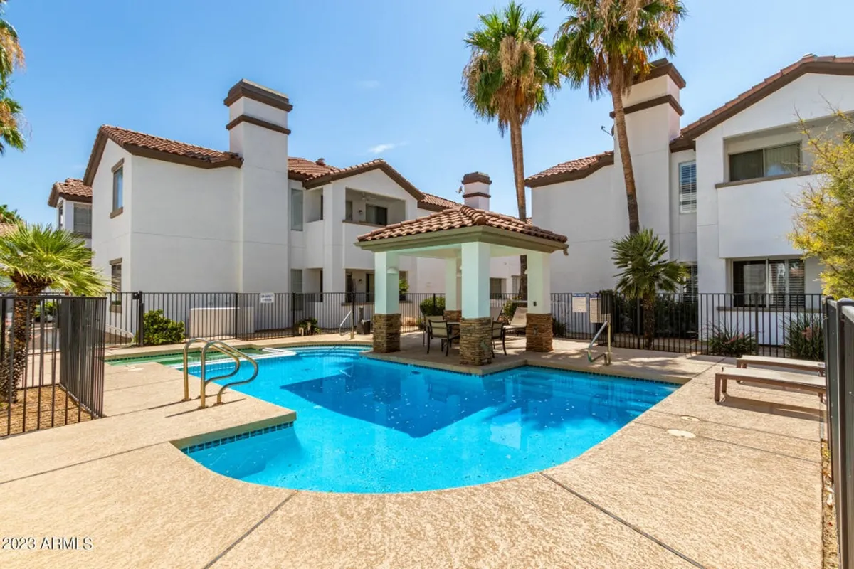 A vibrant community pool scene featuring a sparkling swimming pool, palm trees, and a covered seating area. The space looks inviting for swimming, sunbathing, socializing, or relaxing with friends.