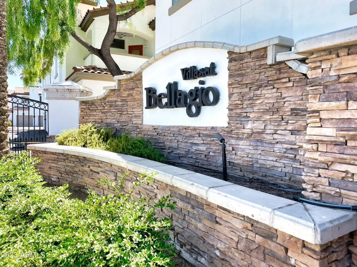 An inviting exterior view of the Villas at Bellagio sign set against a stone wall and surrounded by lush greenery. The entrance conveys a welcoming atmosphere and hints at the secure, gated nature of the community.