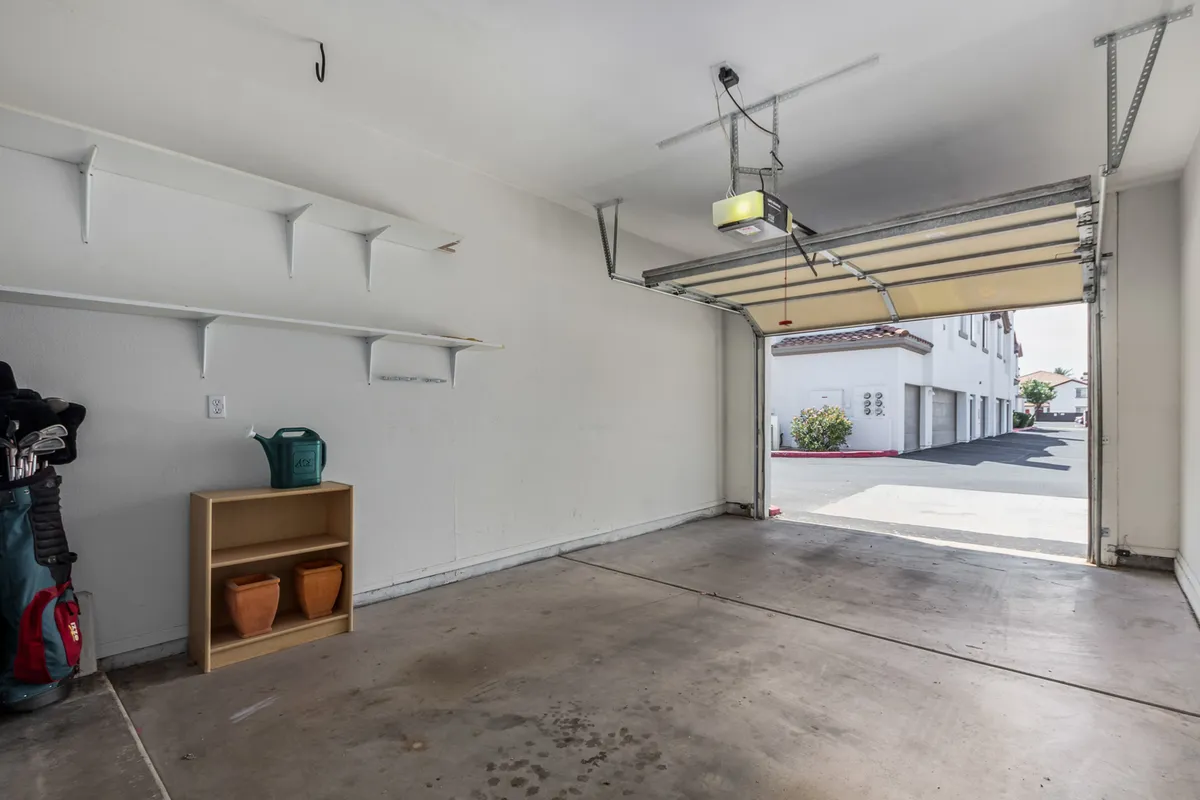 A private one-car garage featuring a sturdy garage door, built-in shelves for storage, a storage unit, and potted plants. The space is clean, organized, and clearly dedicated to both secure vehicle parking and practical storage needs.
