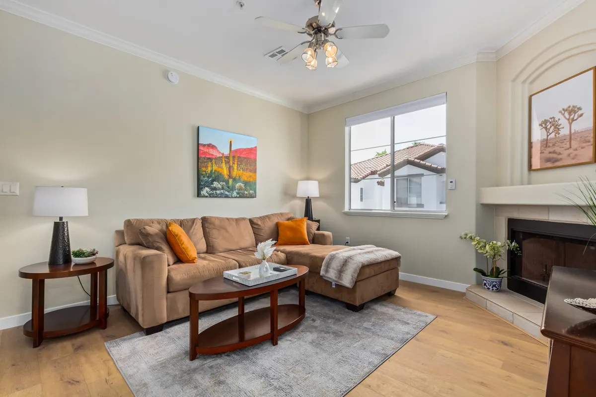 A cozy and inviting living room scene featuring a comfortable sofa, a coffee table set for relaxation, stylish artwork on the walls, a large window allowing in sunset light, and a welcoming fireplace.