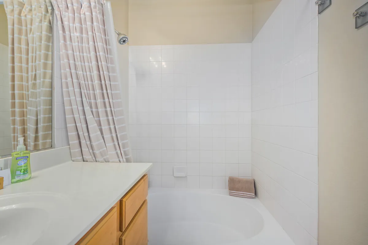 A modern bathroom with a clean vanity, a mirror above, and a tub/shower partially visible beyond a shower curtain—offering a soothing, spa-like environment ideal for self-care routines.