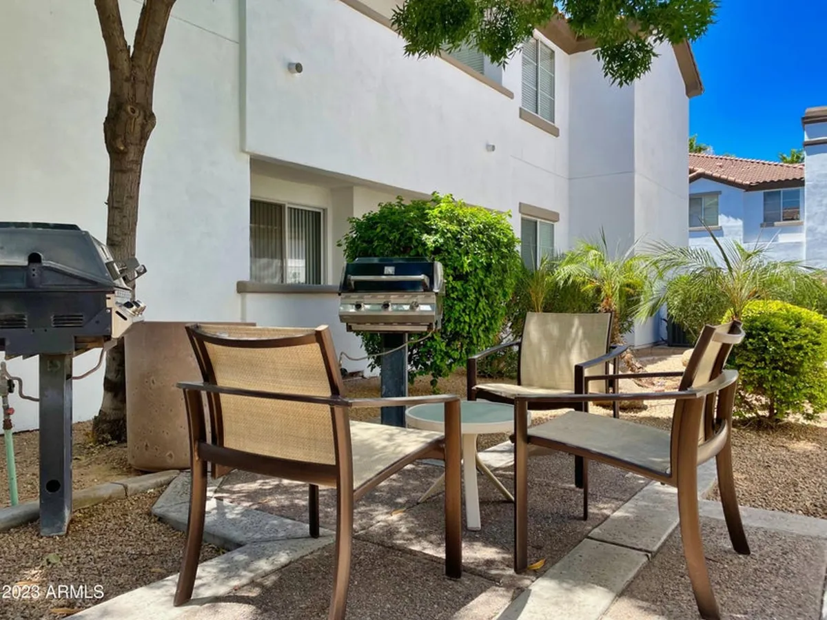 A casual BBQ area with patio chairs, a grill, and green shrubbery, perfect for sunny afternoons and evening cookouts. The setting is ideal for social gatherings and alfresco dining in the privacy of the community.