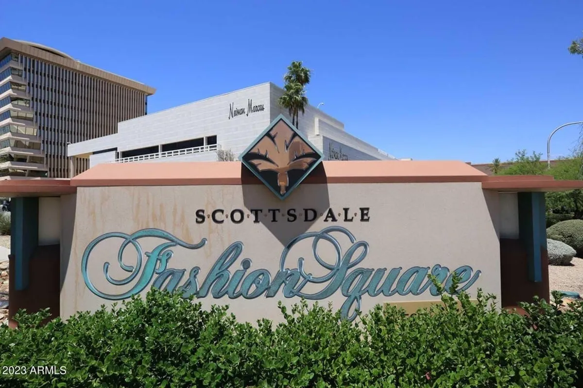 This exterior shot highlights the Scottsdale Fashion Square sign with a modern building and green shrubbery, representing the vibrant, amenity-rich surroundings near the community. The scene is lively, emphasizing easy access to shopping, dining, and social activities.